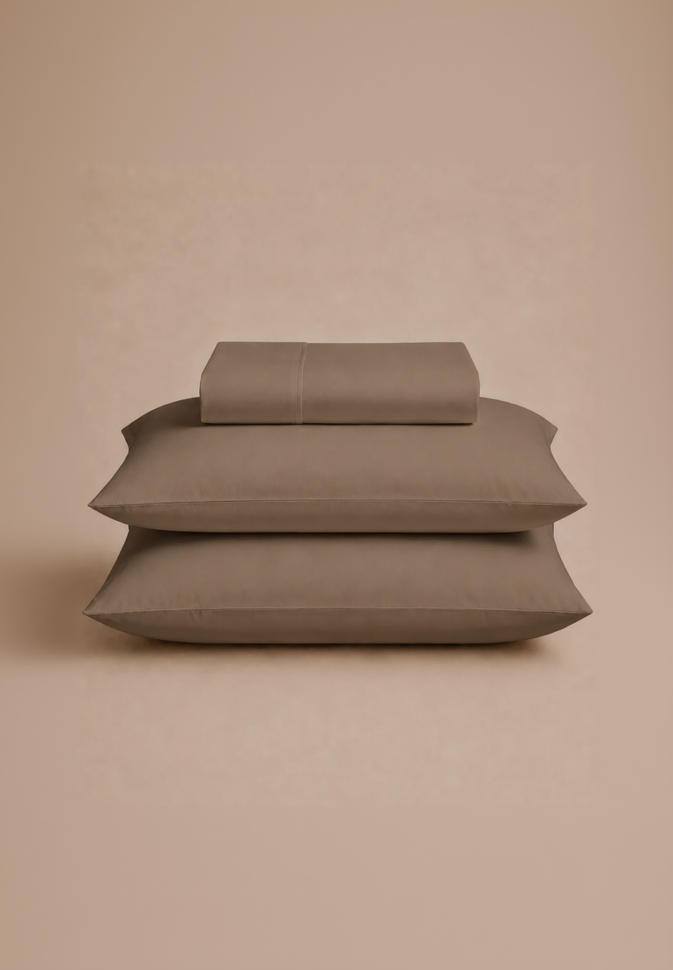 A stack of three pillows in a solid taupe-brown color, with the top pillow folded back to show the fabric texture, set against a matching warm beige background.